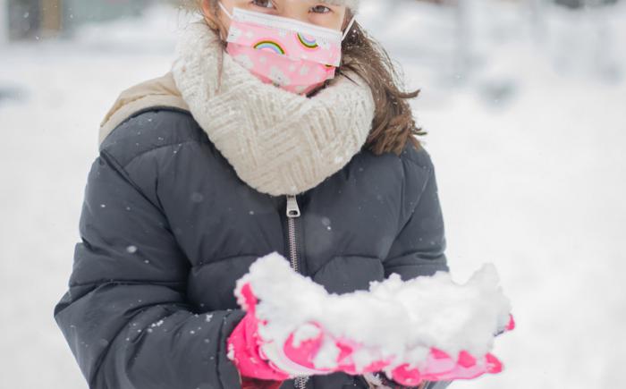 A child in cold-weather clothing holds snow