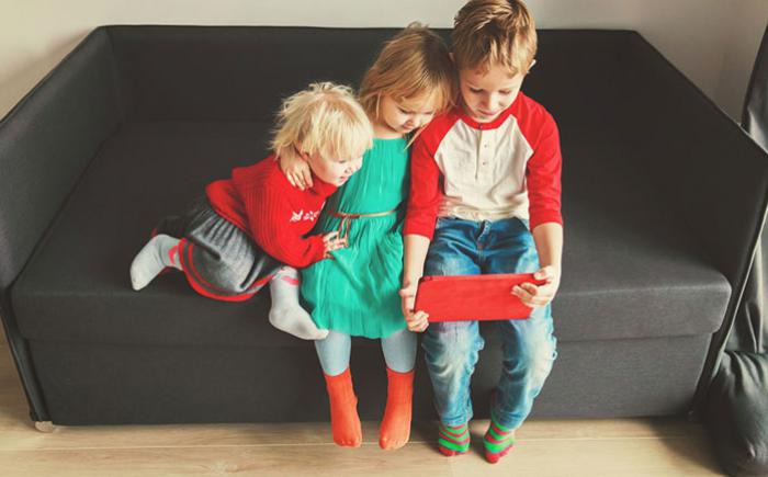 Three children on a loveseat looking at a mobile device