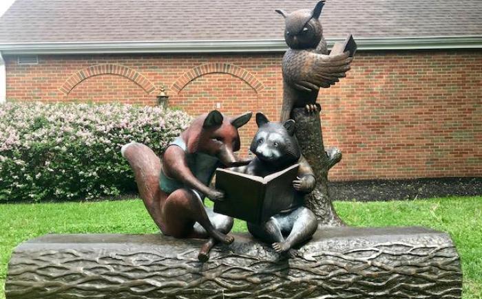 Reading with Friends sculpture portraying a fox, raccoon and owl reading on a log