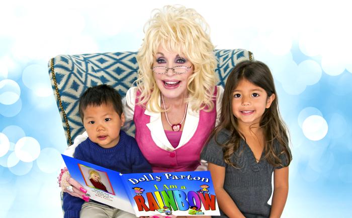 Dolly Parton sitting in a chair reading a book next to two children.