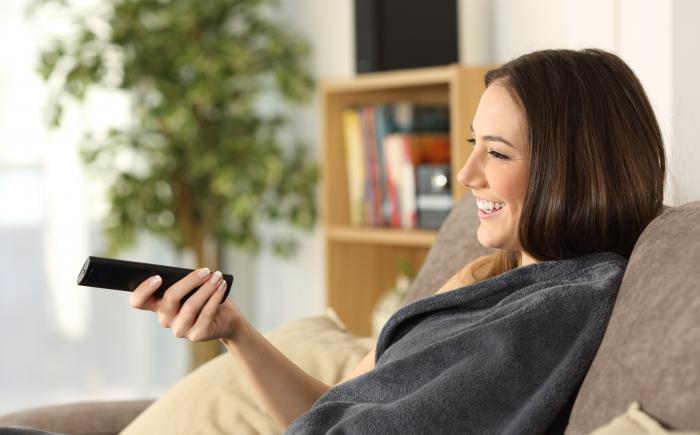 Woman on couch wrapped in blanket holding a remote control