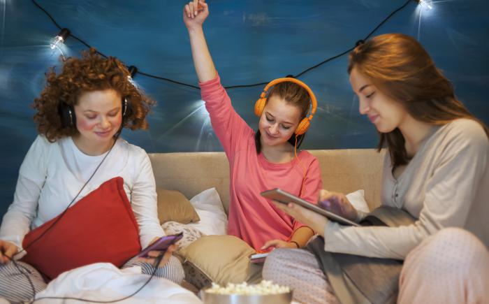 Three girls wearing headphones with smartphones and tablets