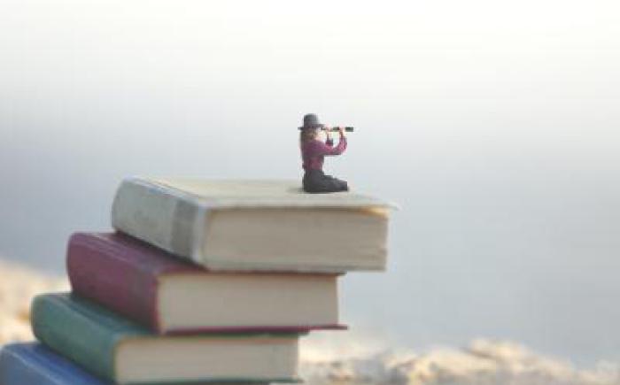 Woman sitting on pile of books looking through spyglass into the distance