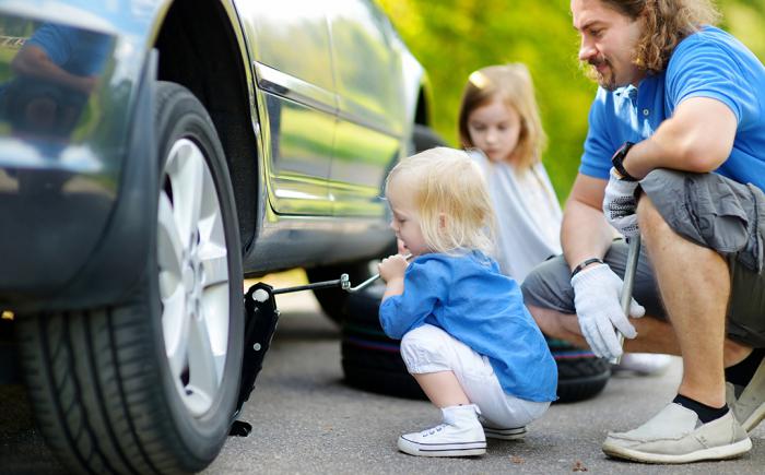 Father observing daughter using jack on car