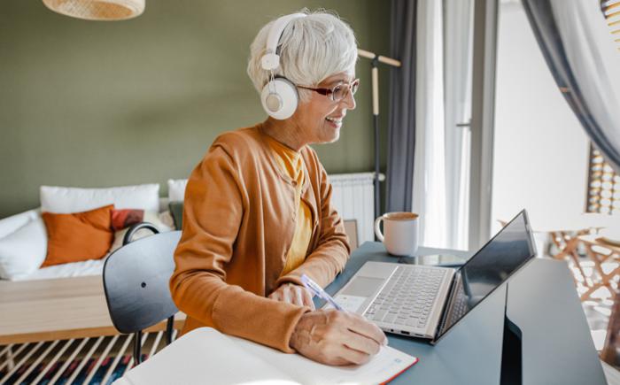 Woman at a laptop writes in a notebook