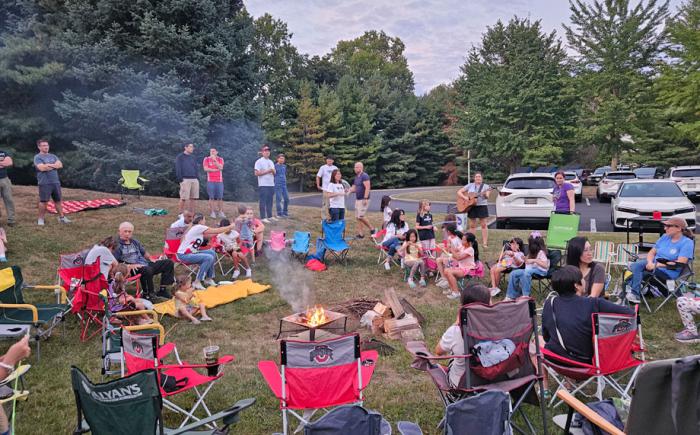 A group of people sitting in folding chairs around a campfire in the Northwest Library backyard.
