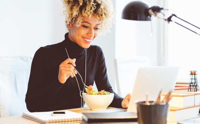 Woman eating salad and looking at a laptop