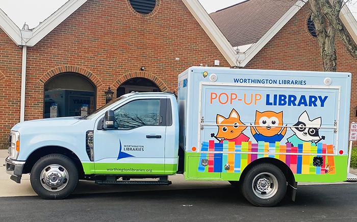 Light blue truck with images of cartoon library mascots along the side