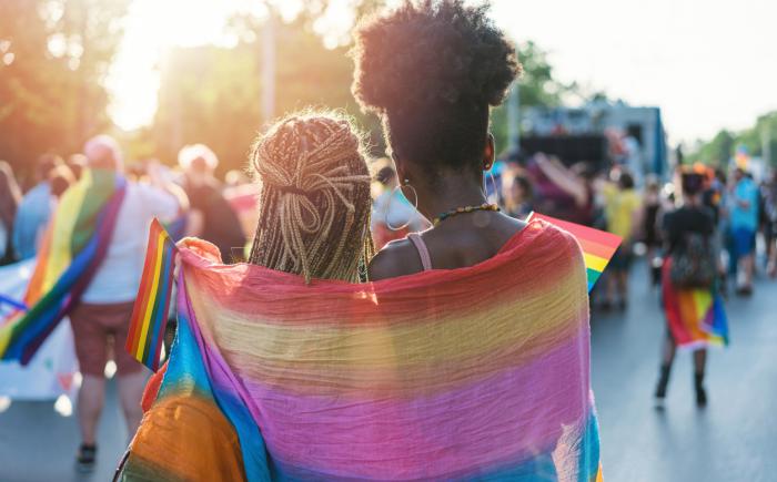 Two people wrapped in a rainbow-colored scarf