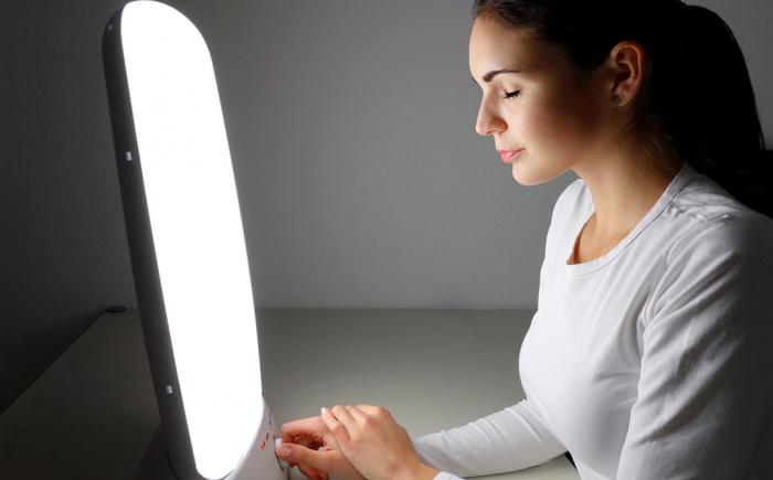 Woman using light therapy lamp with eyes closed