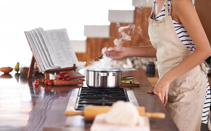 Woman at stove holding spoon over sauce pan