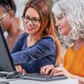 Woman points to a computer monitor while another woman sits at a keyboard