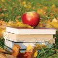 An apple sits atop a stack of books surrounded by grass and leaves