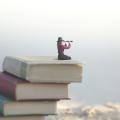 Woman sitting on pile of books looking through spyglass into the distance