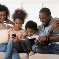 Family of four sitting on couch reading on devices