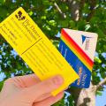 Hand holding Dawes Arboretum pass and library card against green leafy tree and blue sky