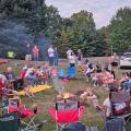 A group of people sitting in folding chairs around a campfire in the Northwest Library backyard.