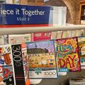 Shelf with puzzle boxes on display and a sign that reads Piece it Together