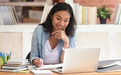 Young adult taking notes while looking at a laptop