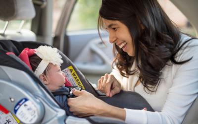 A young woman putting a baby into a car seat