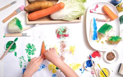 Small hands surrounded by paints and various vegetables