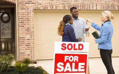Woman giving a couple keys near home for sale sign
