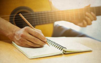 Man writing in a notebook, a guitar on his lap