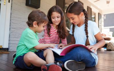 Three children looking at a book outdoors