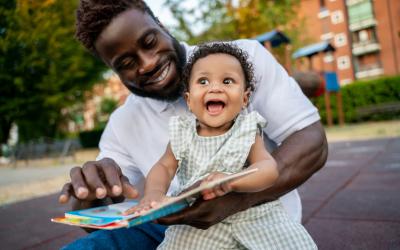 Man holding smiling baby on lap reading a board book