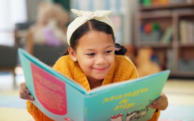Smiling girl lying on stomach reading a picture book
