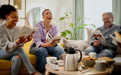 Three people holding books gathered around a coffee table laughing
