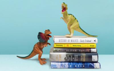 Dinosaur toys standing on stack of books