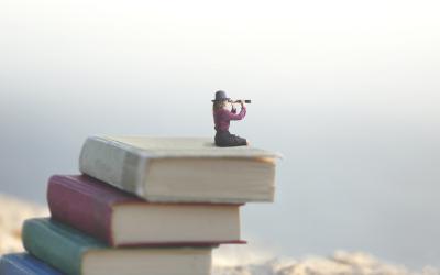 Woman sitting on pile of books looking through spyglass into the distance