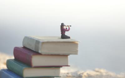 Woman sitting on pile of books looking through spyglass into the distance