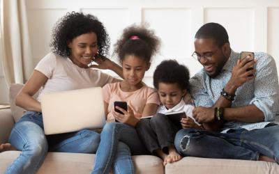 Family of four sitting on couch reading on devices