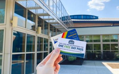 Hand holding community center pass and library card with the Worthington Community Center exterior in the background