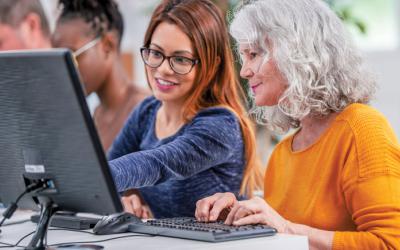 Woman points to a computer monitor while another woman sits at a keyboard