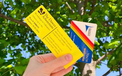Hand holding Dawes Arboretum pass and library card against green leafy tree and blue sky