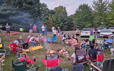 A group of people sitting in folding chairs around a campfire in the Northwest Library backyard.