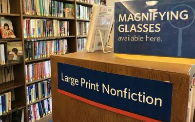 Signs that say: Magnifying glasses available here; and Large Print Nonfiction