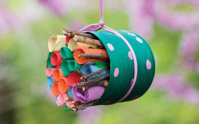 A small, colorful paper bug hotel filled with rolled up pieces of paper.