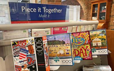 Shelf with puzzle boxes on display and a sign that reads Piece it Together