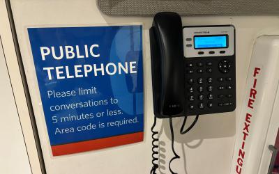 Telephone on wall next to a sign with details about use of public telephone