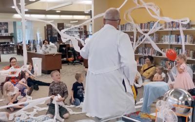 An adult in a lab coat teaching children science.