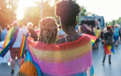 Two women wrapped in a rainbow-colored scarf