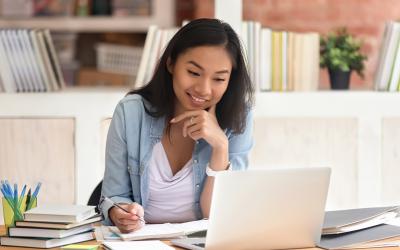 Smiling woman look at laptop and taking notes at a desk