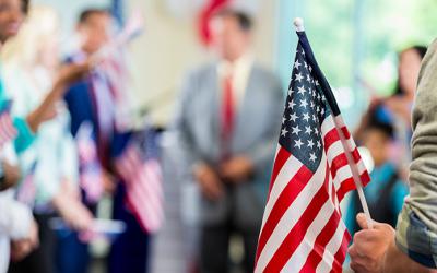 Hand holding small American flag with gathering of people behind