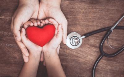 Two pairs of hands holding a heart shape next to a stethoscope