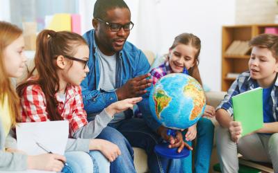 Teacher surrounded by students looking at a globe
