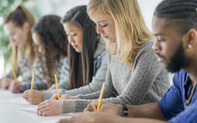 Students sitting at a table writing with pencils